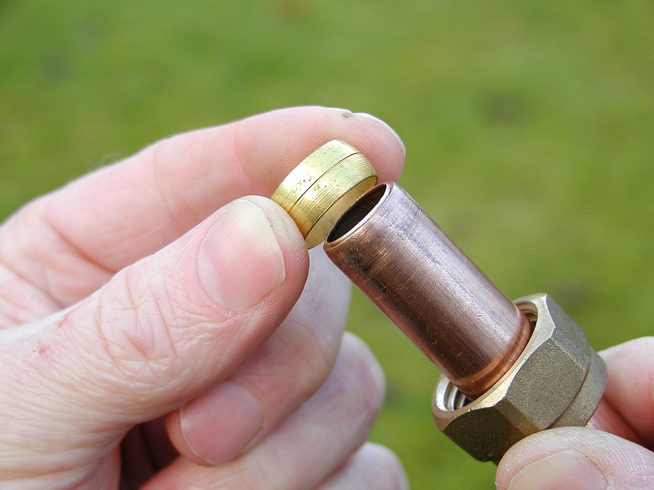 Hand holding a copper pipe fitting with a brass olive ring