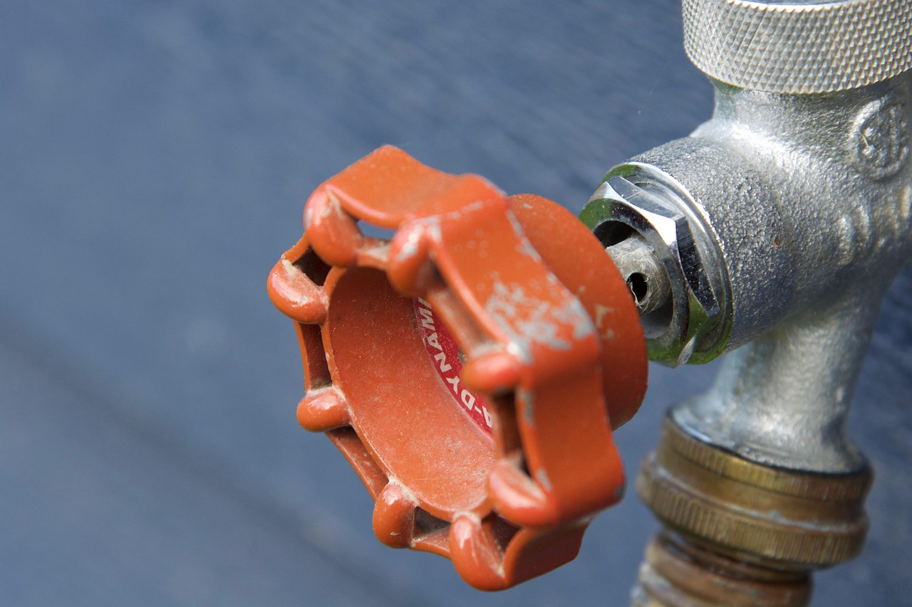 Red valve knob on a galvanised drain fitting against blue-painted timber
